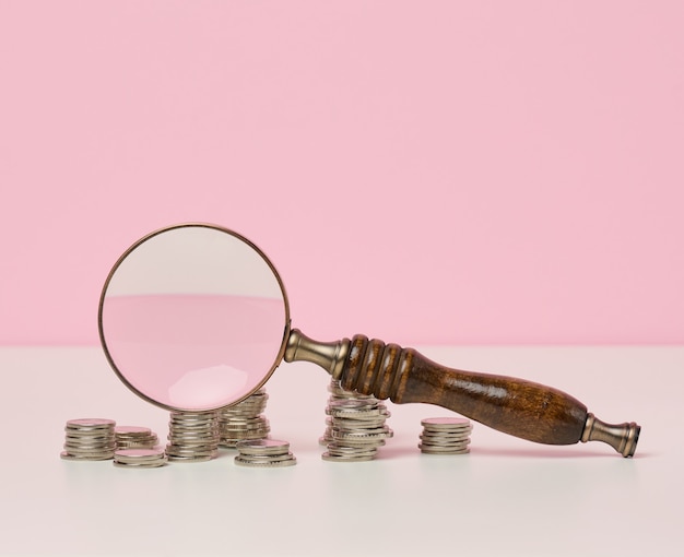 Wooden magnifier and white coins on the table. Income growth concept, high percentage of investment. Search for new sources of income, subsidy