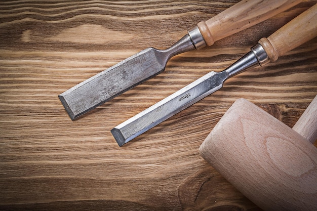 Wooden mallet flat chisels on vintage wood board construction concept.