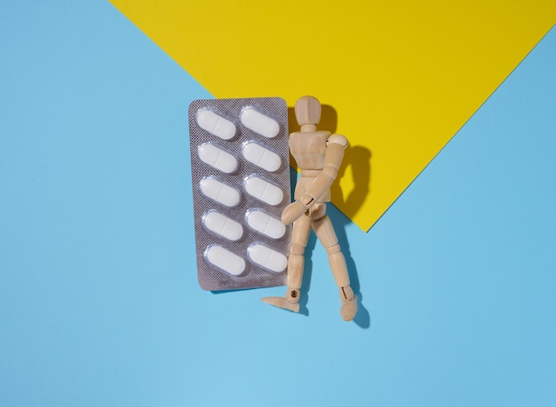 Wooden mannequin leaning against a blister of white pills on a blue and yellow background