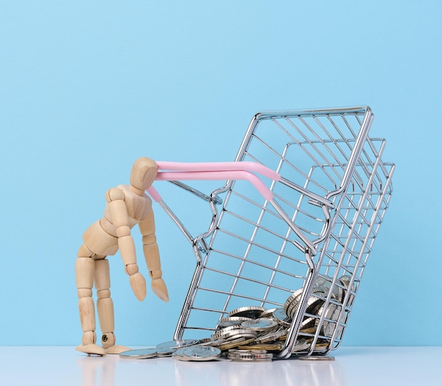 Wooden mannequin and loose change from a miniature shopping basket on a blue background