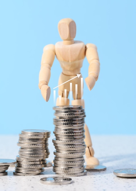 Wooden mannequin and a stack of coins on a blue background Business indicators growth concept income growth