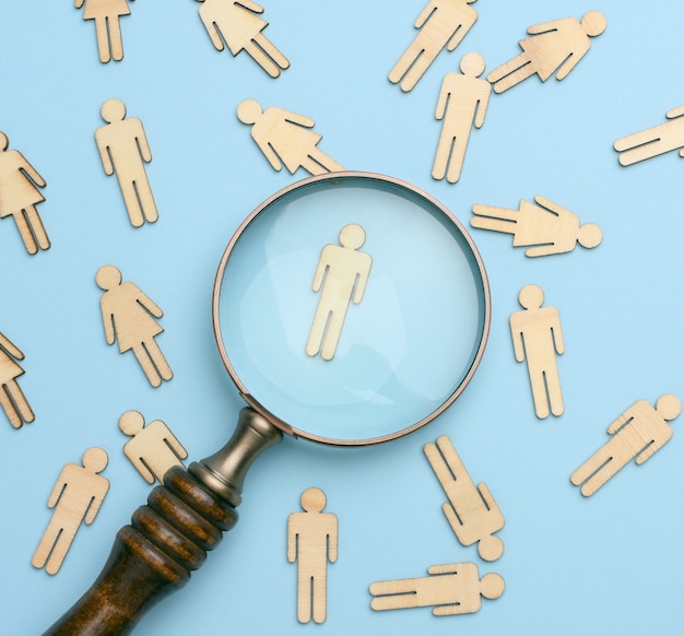 Photo wooden men and a magnifying glass on a blue background. recruitment concept, search for talented and capable employees, career growth, flat lay