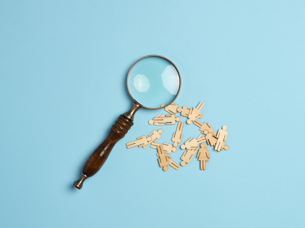 Wooden men and a magnifying glass on a blue background Recruitment concept search for talented and capable employees career growth flat lay