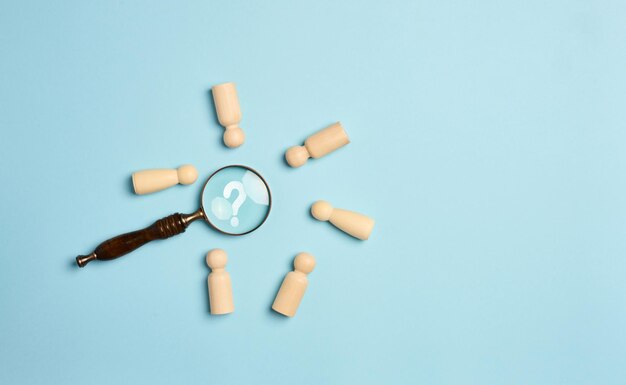 Wooden men and a magnifying glass on a blue background Recruitment concept search for talented and capable employees career growth flat lay