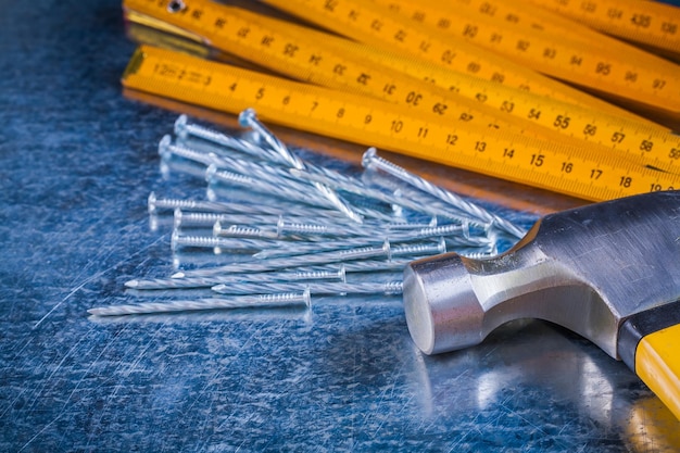 Wooden meter variety of metal nails and claw hammer on scratched metallic surface construction concept