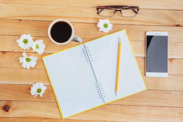 On wooden  notebook pencil, coffee and flowers.