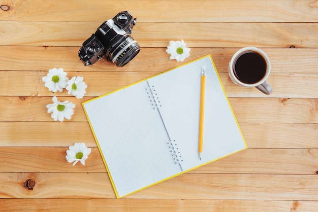 On wooden  notebook pencil, coffee and flowers.