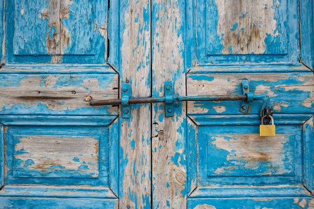 Wooden peeled blue door closed locked aged for background Rusty latch and padlock Close up view