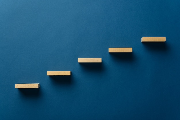 Wooden pegs place over navy blue background in a stairway like structure in a conceptual image. With copy space.