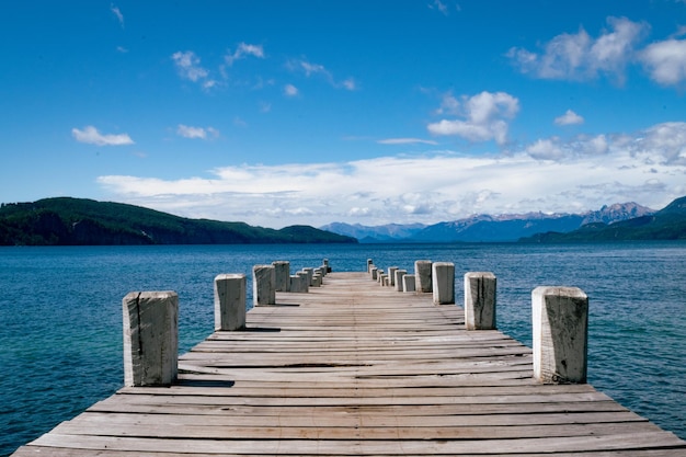 a wooden pier with a blue sky and a mountain in the background