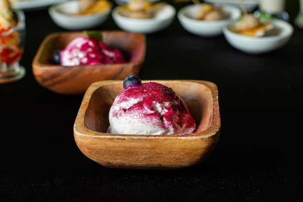 Wooden plate of blueberry ice cream In the background are catering dishes Front view