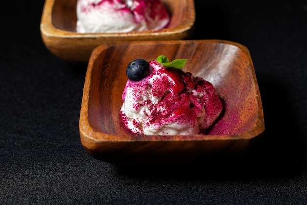 Wooden plate of blueberry ice cream with fresh berries on black table Beautiful colored topping