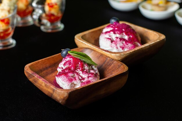 Wooden plate of blueberry ice cream with fresh berries colored topping In background are catering