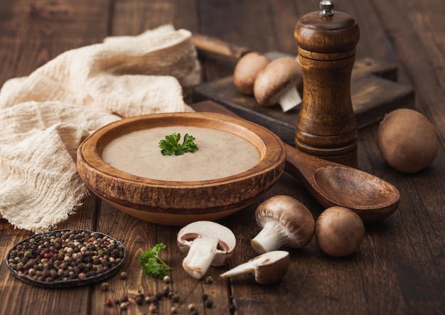 Wooden plate of creamy chestnut champignon mushroom soup with wooden spoon pepper and kitchen cloth on wooden board