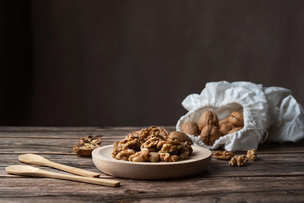 Wooden plate filled with peeled walnuts and sack of walnuts in shell on a wooden table