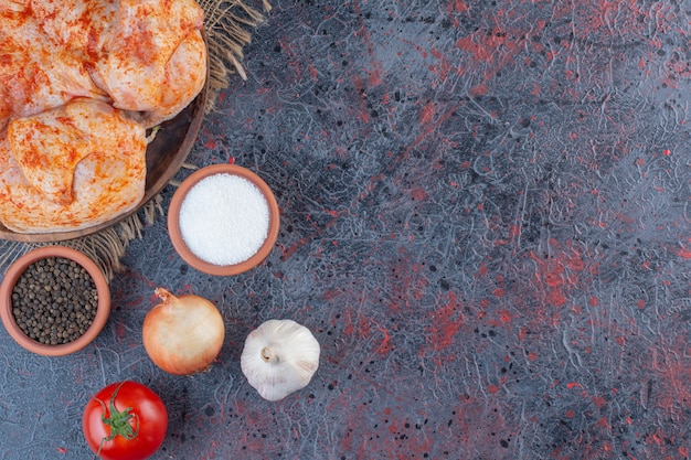 Wooden plate of marinated whole chicken on marble surface