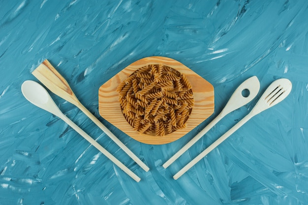 Wooden plate of raw dry fusilli on marble surface