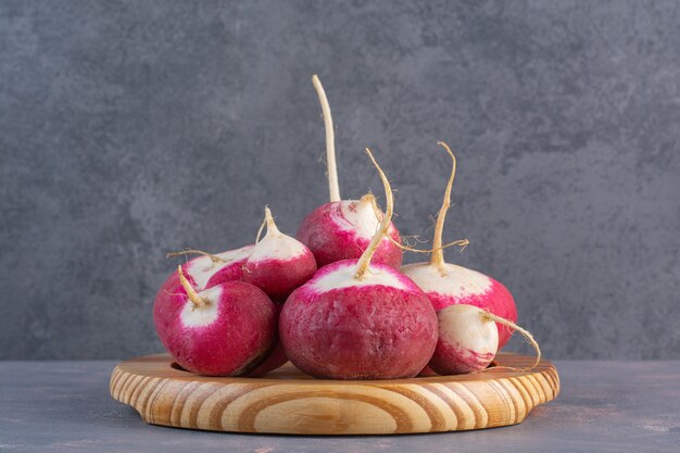 Wooden plate of summer harvested red fresh radishes on stone surface