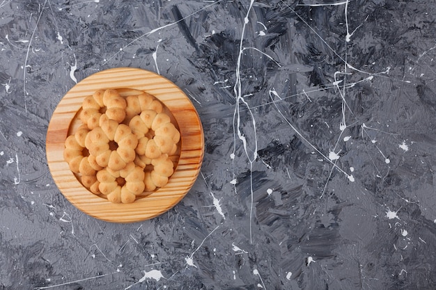 Wooden plate of sweet flower shaped cookies on marble background. 