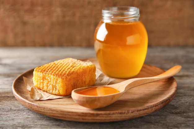 Wooden plate with delicious honey and fresh honeycomb on table