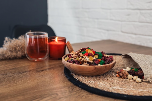 Wooden plate with dried fruits and candied fruits in the kitchen against the background of tea and a candle