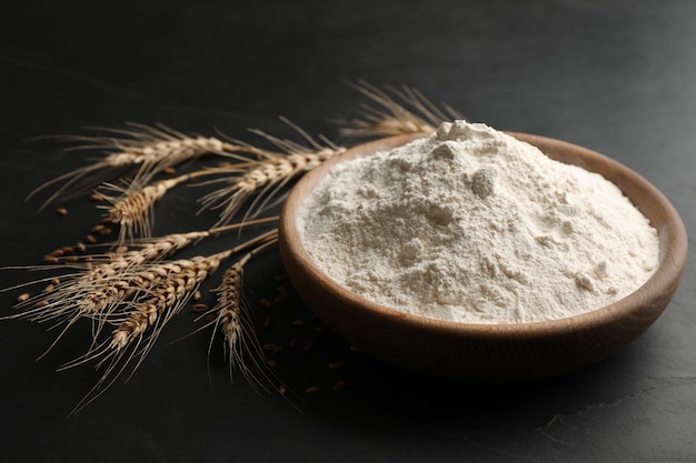 Photo wooden plate with flour and wheat ears on black table