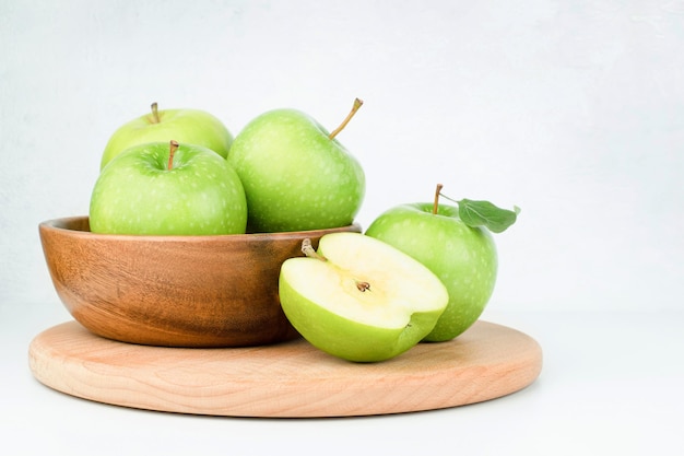 Wooden plate with fresh green apples on a light background