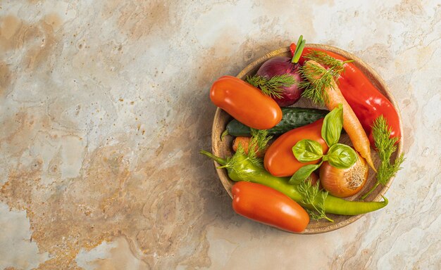 Wooden plate with fresh vegetables green pepper tomato onion carrot cucumber basil dill on brown background top view rustic concept