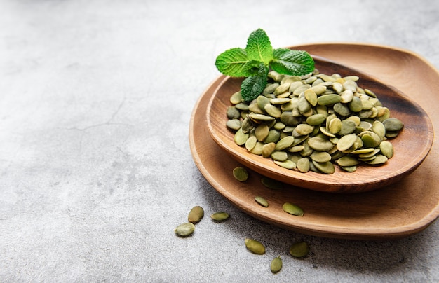 Wooden plate with pumpkin seeds on a gray concrete surface