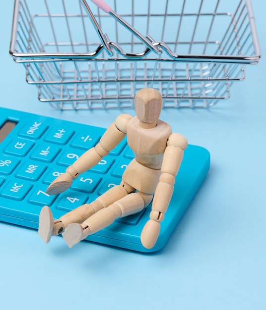 A wooden puppet and a blue calculator behind a miniature shopping basket