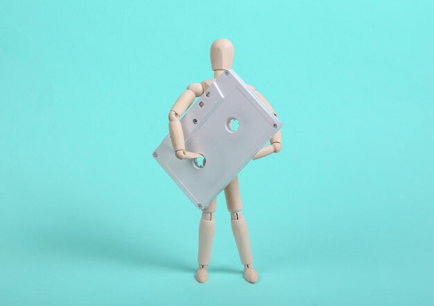 Wooden puppet holding white audio cassette on blue background