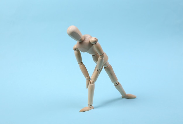 Wooden puppet injured with leg pain on blue background