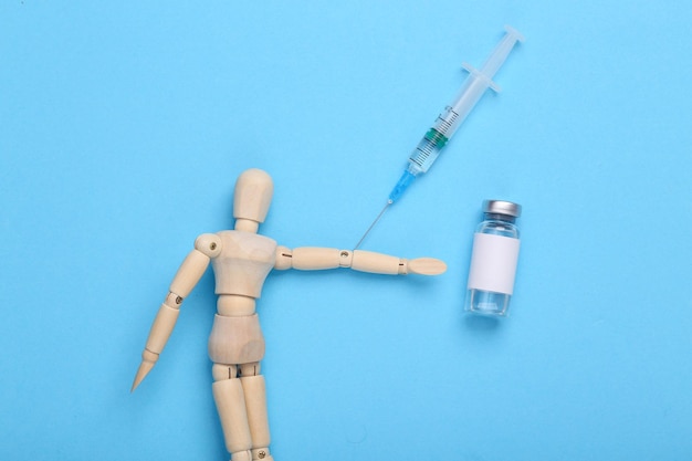 Photo wooden puppet makes a vaccine on a blue background