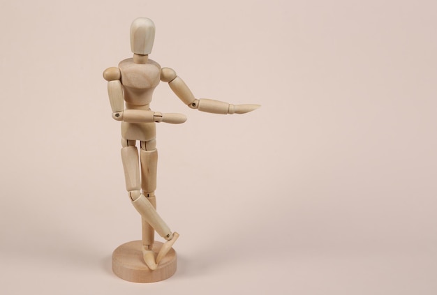 Wooden puppet mannequin shows on the empty space for your text on beige background Copy space