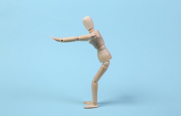 Wooden puppet practices squats against blue background. Aerobics concept