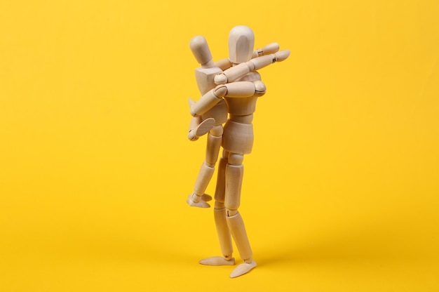 Wooden puppets hug on a yellow background. Parental love concept