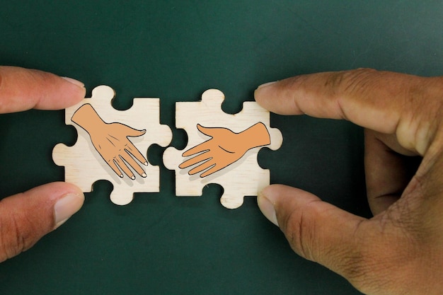 Photo wooden puzzle with two shaking hands icons the concept of deal or agreement business partner