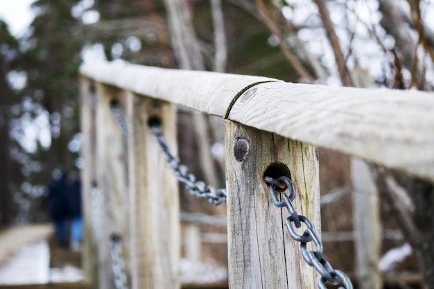 A wooden railing with a metal chain in the middle and green trees in the background