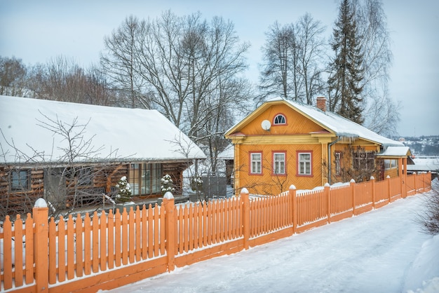 Wooden residential yellow house and a fence on Nikolskaya Street in Plyos in the light of a winter day under a blue sky