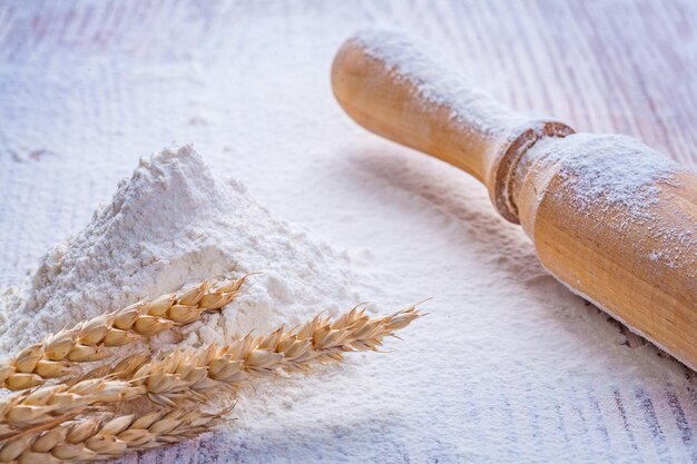 Wooden rolling pin and heap flour with ears of wheat on vintage board