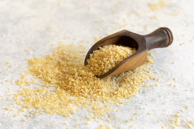 Wooden scoop of Dry uncooked bulgur wheat grain close up copy space Healthy food