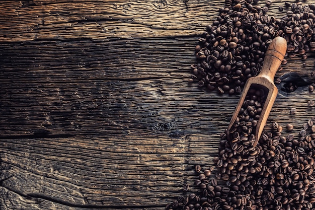 Wooden scoop full of coffee beans on old oak table.