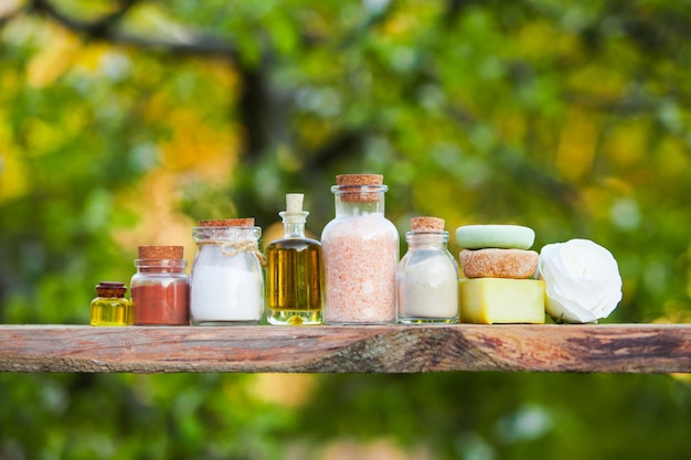 Wooden shelf with organic cosmetics close up outdoors. Bottles and hard creams and shampoo with flower, copy space. Nature design