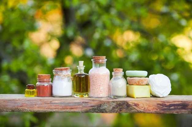 Wooden shelf with organic cosmetics outdoors. Bottles and hard soap with flower, place for text