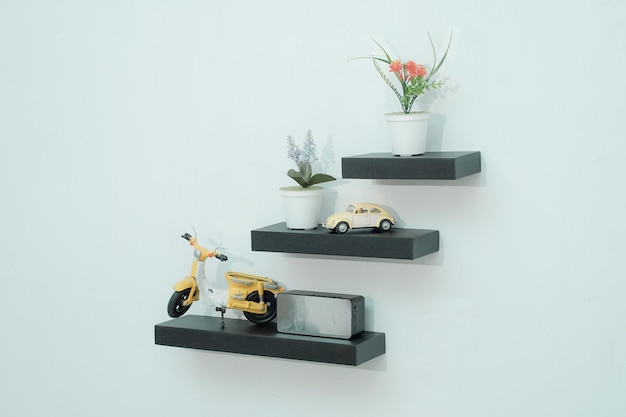 Wooden shelves with beautiful plants alarm clock toy cars and books on a light wall