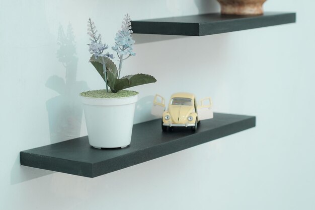 Wooden shelves with beautiful plants alarm clock toy cars and books on a light wall