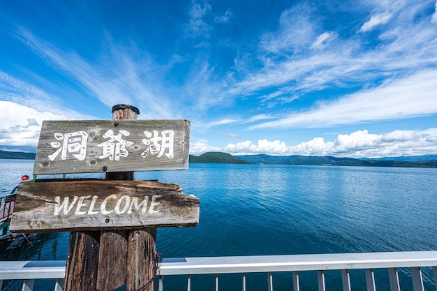 A wooden sign that says welcome on it with the water in the background.