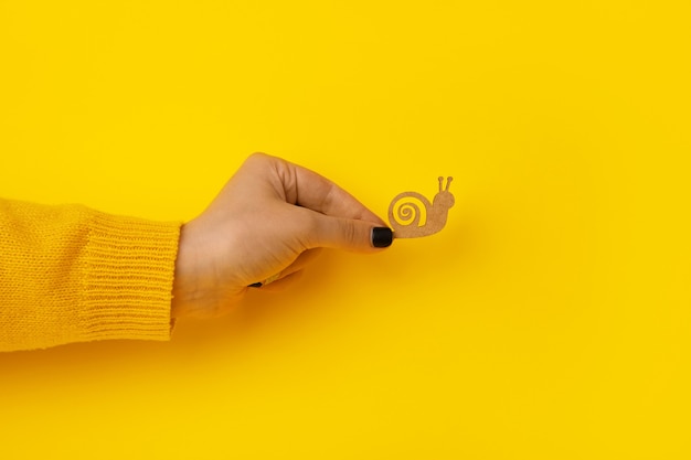 Wooden snail in hand over yellow background, slowness concept