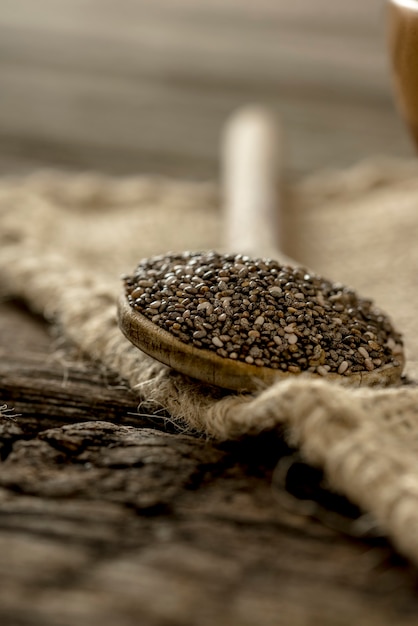 Wooden spoon full of healthy nutritious chia seeds on a burlap sac on a rustic wooden desk.