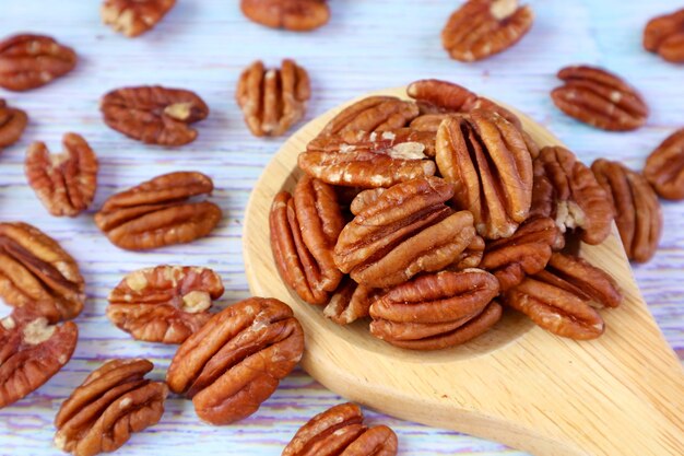 Wooden Spoon Full of Pecan Nuts with Many Kernels Scattered on Pale Blue Wooden Table